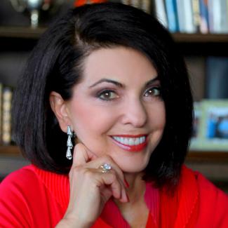 Talia Carner, smiling red top, in front of a bookshelf